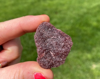 Puede incluir: Un solo caramelo gomoso de color morado oscuro, de forma irregular y textura granulada.