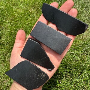 May include: Four black obsidian stones of varying shapes and sizes. The stones are smooth and polished, with a dark, glossy finish.