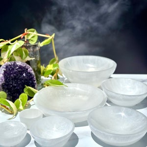 Pu&ograve; includere: Un set di sette ciotole di selenite bianca di diverse dimensioni. Le ciotole sono disposte a semicerchio su una superficie bianca. Le ciotole sono realizzate in selenite, un tipo di cristallo noto per le sue propriet&agrave; calmanti e purificanti.