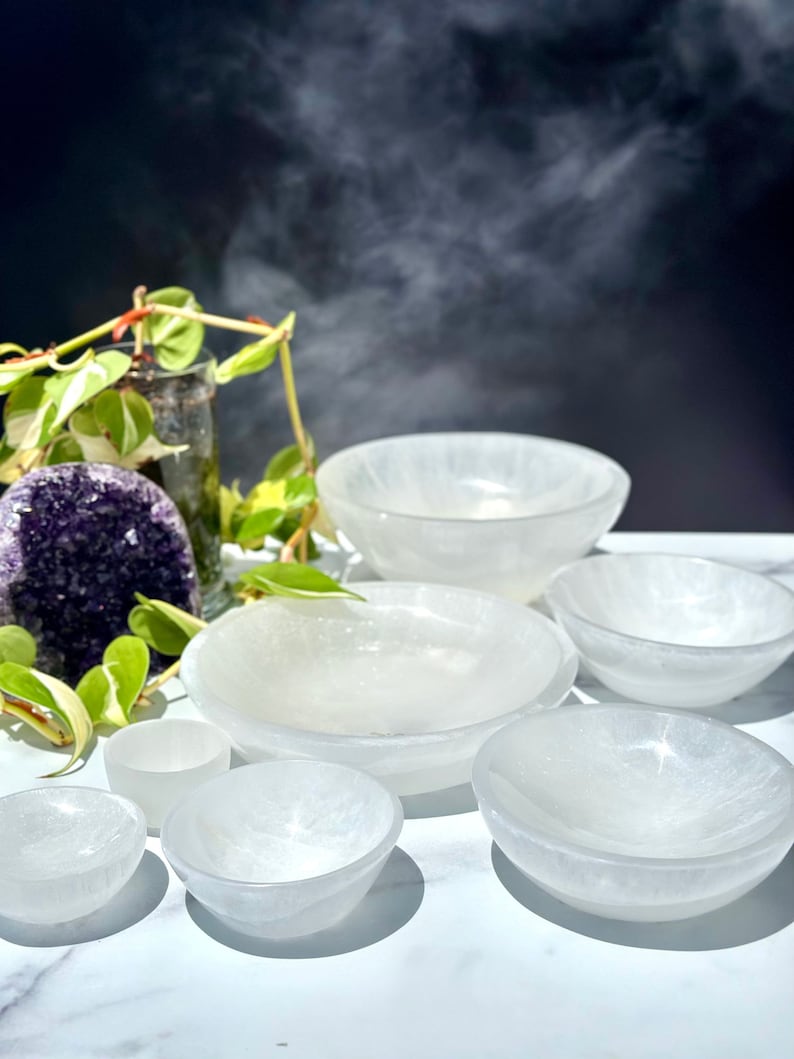 Pu&ograve; includere: Un set di sette ciotole di selenite bianca di diverse dimensioni. Le ciotole sono disposte a semicerchio su una superficie bianca. Le ciotole sono realizzate in selenite, un tipo di cristallo noto per le sue propriet&agrave; calmanti e purificanti.