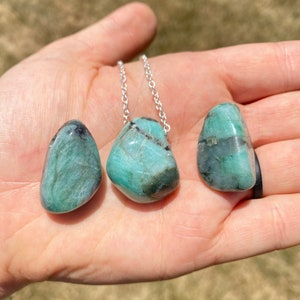 Puede incluir: Tres piedras de esmeralda verde en un collar de cadena de plata. Las piedras son lisas y tienen un acabado natural y pulido.