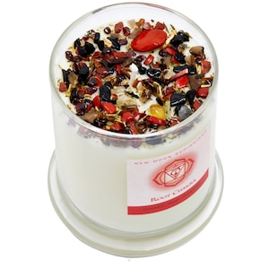 May include: A clear glass jar candle with a white wax base and a red, black, and brown crystal and herb blend. The label reads "New Moon Beginnings Root Chakra Grounded, Secure, Yantra".