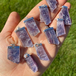 May include: Ten purple lepidolite crystal pendants with silver bail settings. The pendants are various shapes and sizes.