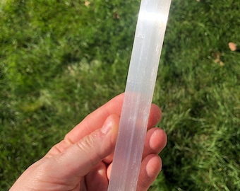 May include: A white selenite wand with a smooth, polished surface. The wand is about 6 inches long and has a rectangular shape.