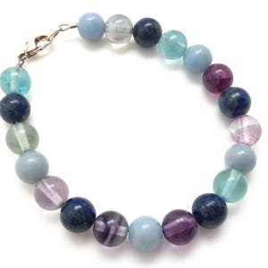 May include: A beaded bracelet featuring a variety of colorful gemstones. The bracelet includes round beads in shades of blue, purple, green, and clear. The clasp is silver-colored. This piece of jewelry is suitable for everyday wear.