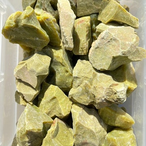 May include: A collection of green moss agate rough stones. The stones are various sizes and shapes, with a rough, natural texture.