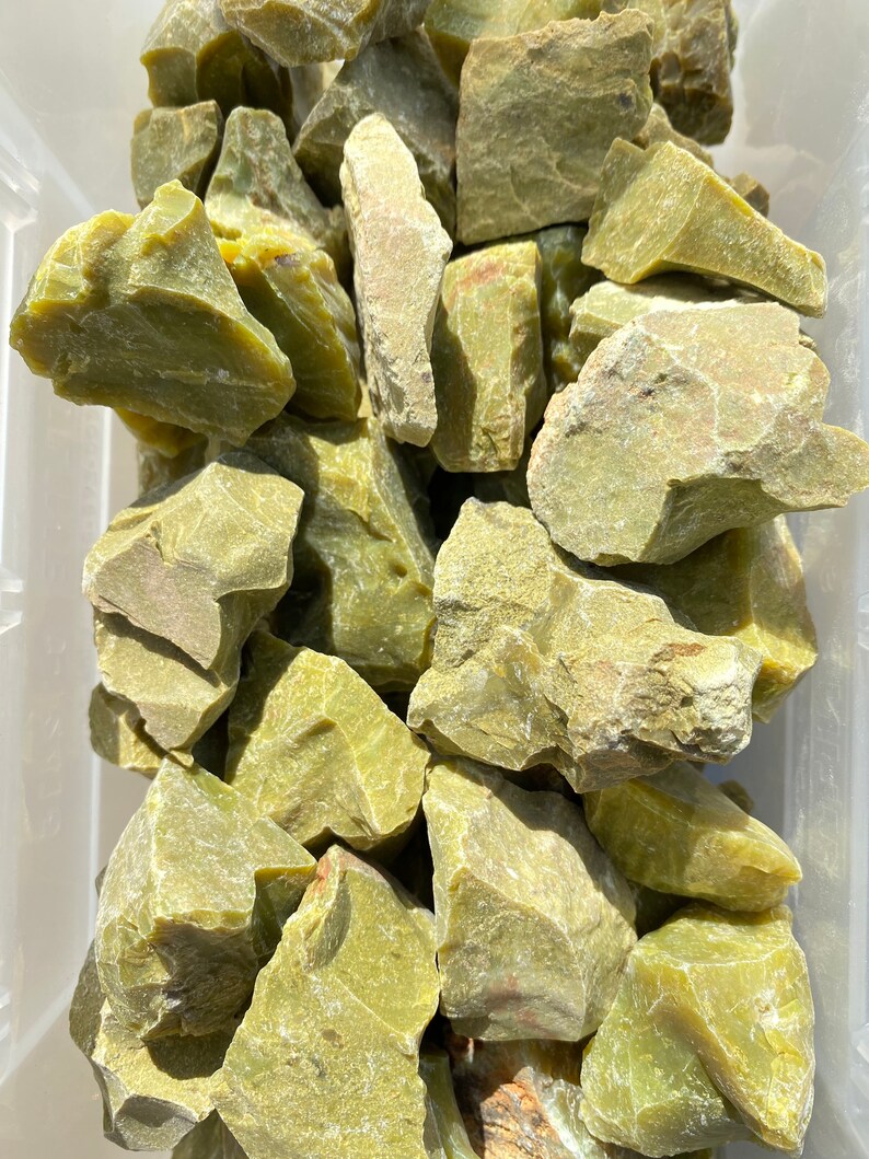 May include: A collection of green moss agate rough stones. The stones are various sizes and shapes, with a rough, natural texture.