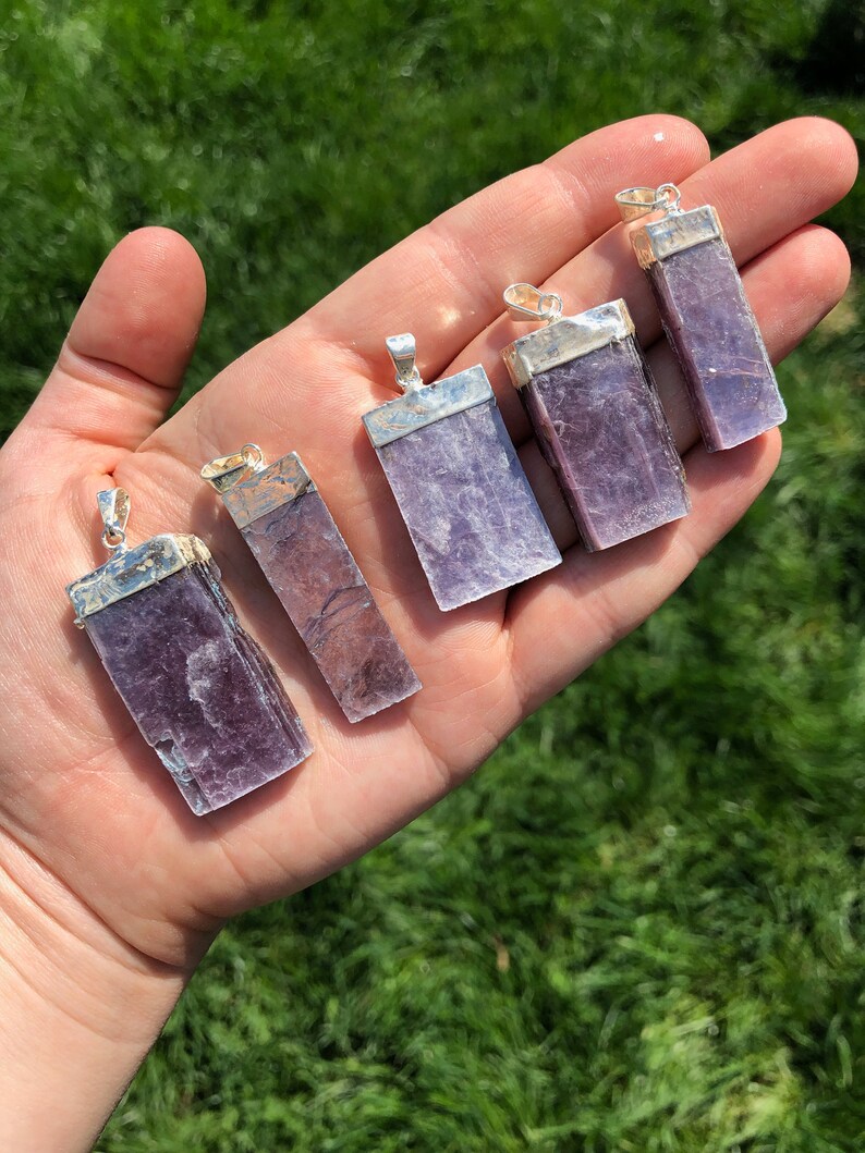 May include: Six purple lepidolite crystal pendants with silver settings. The pendants are rectangular in shape and have a smooth, polished finish.