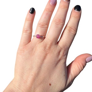 May include: A silver ring with a pink gemstone. The ring is on a person's finger.