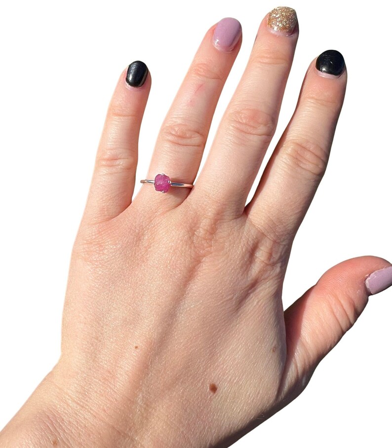 May include: A silver ring with a pink gemstone. The ring is on a person's finger.