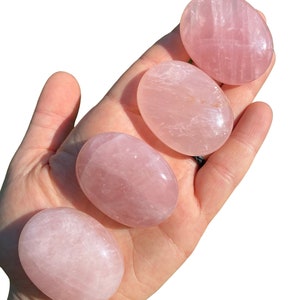 Pu&ograve; includere: Quattro pietre di quarzo rosa lisce, di forma ovale e di diverse dimensioni, mostrate su una mano.