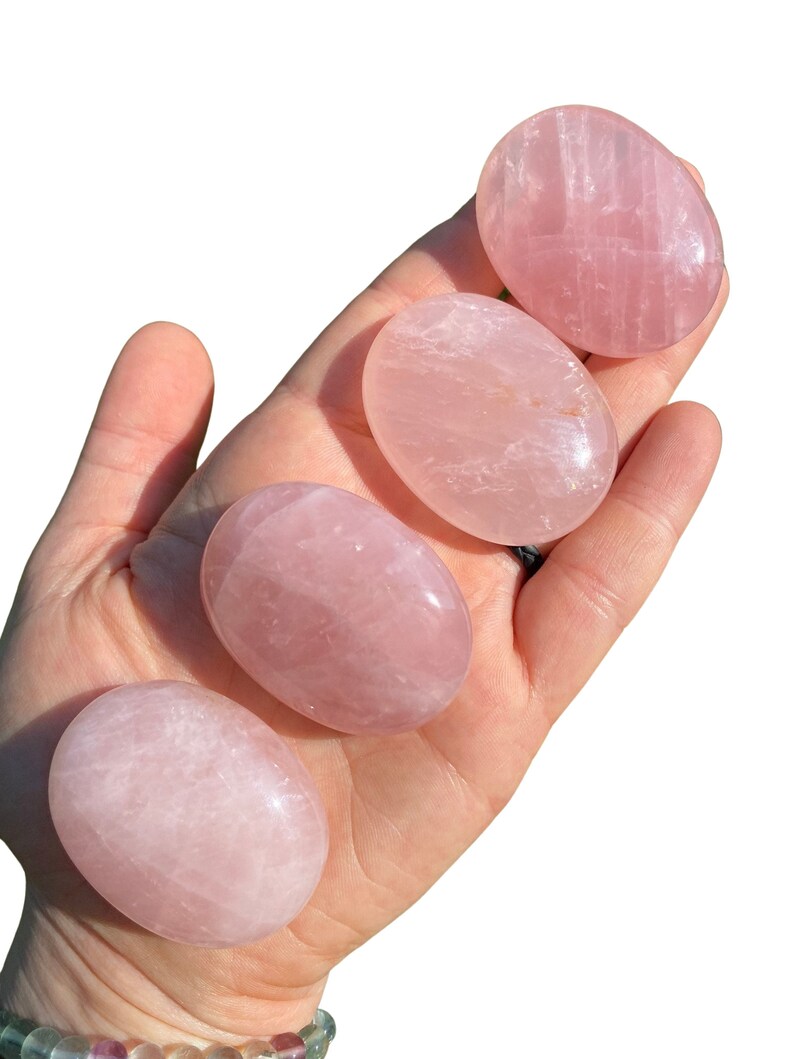 Pu&ograve; includere: Quattro pietre di quarzo rosa lisce, di forma ovale e di diverse dimensioni, mostrate su una mano.