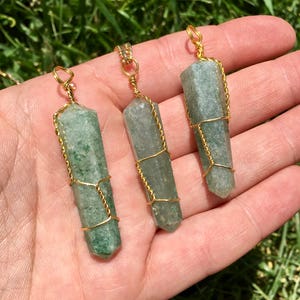 Puede incluir: Tres colgantes de cristal hexagonal verde, semitransl&uacute;cido, cada uno envuelto en un fino alambre de color dorado. Los cristales presentan inclusiones naturales y variaciones de color, con un lazo de alambre dorado en la parte superior.