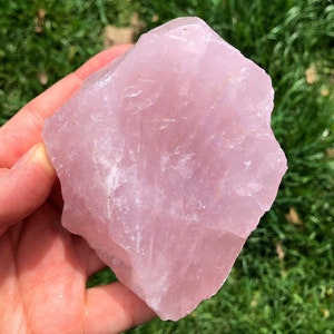 May include: A large, rough-cut, pink rose quartz crystal. The crystal has a natural, irregular shape and a translucent, pale pink color.