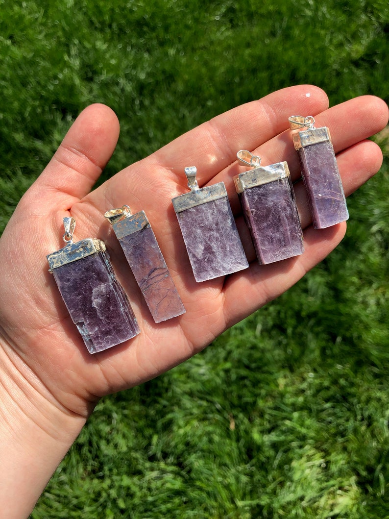 May include: Six purple lepidolite crystal pendants with silver bail settings. The pendants are rectangular in shape and have a natural, raw finish.
