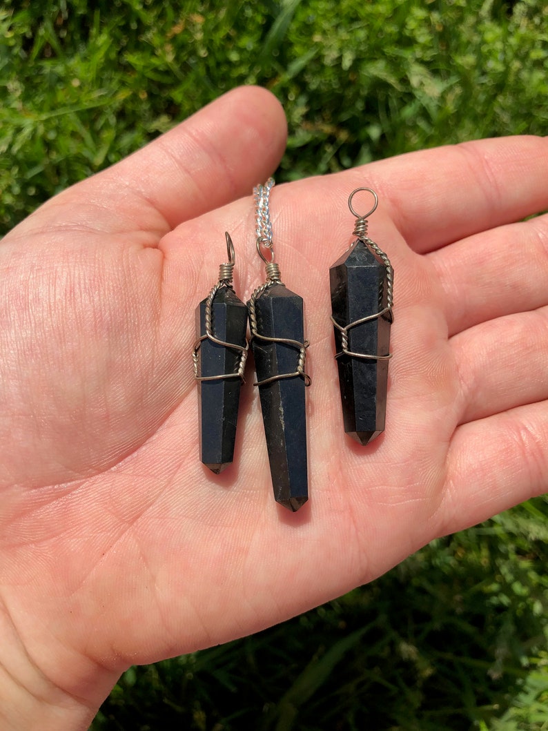 Pode incluir: Tr&ecirc;s pingentes de cristal de obsidiana preta envoltos em fio de prata. Os pingentes s&atilde;o de tamanhos diferentes e est&atilde;o pendurados em correntes de prata.