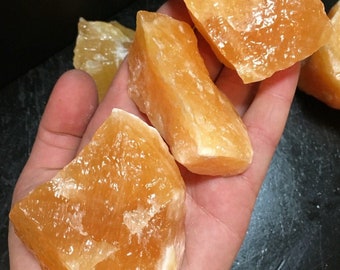 May include: A collection of four orange calcite crystal chunks. The crystals are rough and have a natural, unpolished look.
