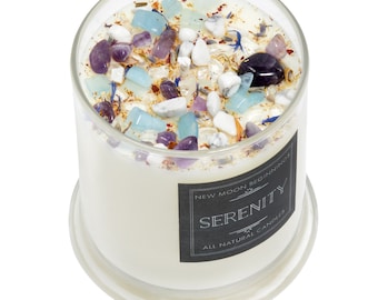 May include: A glass jar candle with a white wax base and a black label that reads "New Moon Beginnings Serenity All Natural Candles". The jar is filled with various crystals and stones, including amethyst, clear quartz, and aquamarine.