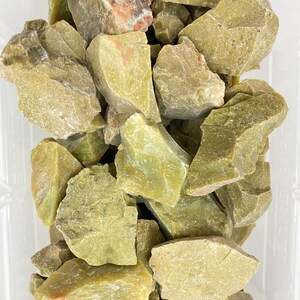 May include: A collection of rough, green, and gray-green jade stones. The stones are various sizes and shapes, and some have a slightly translucent quality.