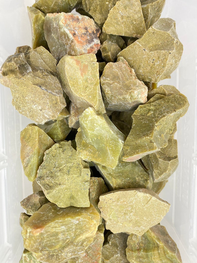 May include: A collection of rough, green, and gray-green jade stones. The stones are various sizes and shapes, and some have a slightly translucent quality.