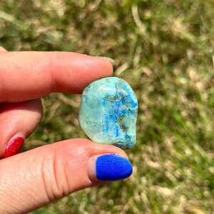 May include: A smooth, light blue and green gemstone with dark blue veins. The stone is tumbled and has a rounded shape.