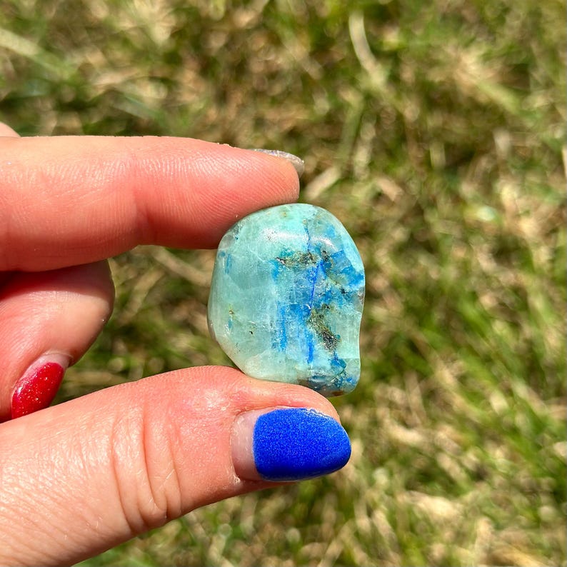 May include: A smooth, light blue and green gemstone with dark blue veins. The stone is tumbled and has a rounded shape.