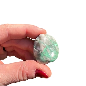 May include: A smooth, green and white gemstone with a mottled pattern. The stone is oval shaped and has a glossy finish.