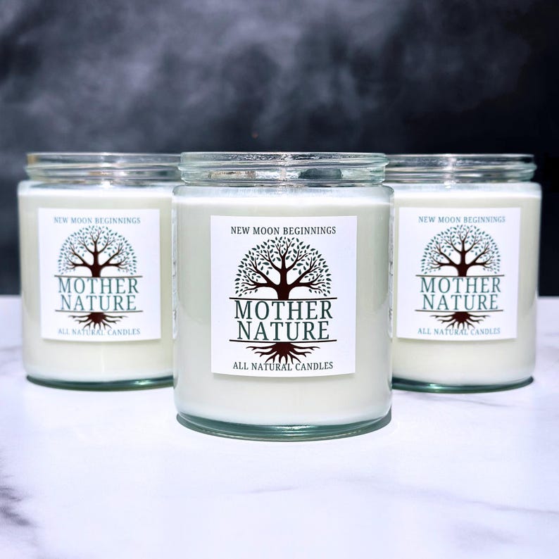 May include: Three glass candle jars with white labels. The labels have a tree design and the text "NEW MOON BEGINNINGS" and "MOTHER NATURE" with the words "ALL NATURAL CANDLES" below.