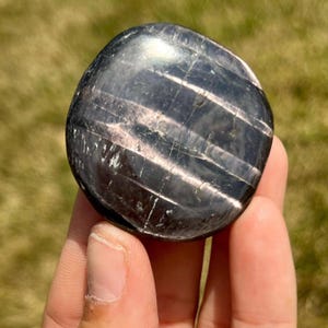 May include: A smooth, black and silver gemstone with a striated pattern. The gemstone is polished and has a reflective surface.