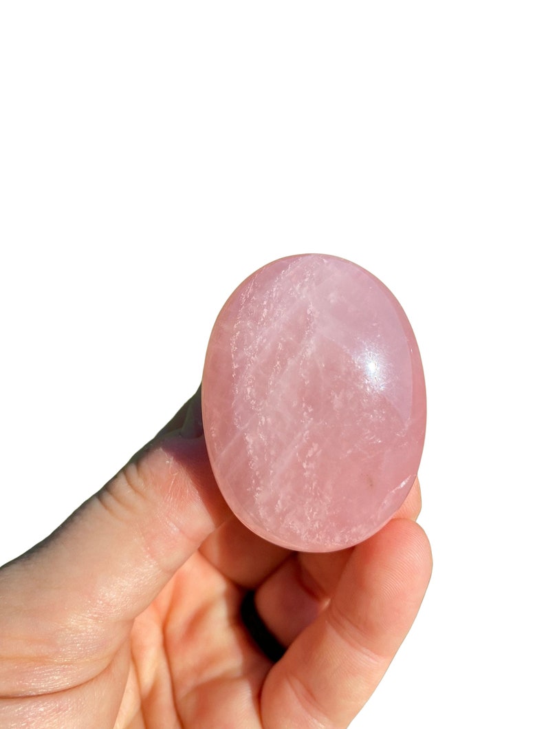 Pu&ograve; includere: Un cristallo di quarzo rosa liscio, di colore rosa pallido, a forma ovale. Il cristallo &egrave; tenuto in una mano.