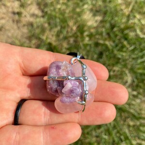 May include: A silver wire cage pendant with a pink and purple amethyst crystal cluster. The cage is adorned with small silver beads.