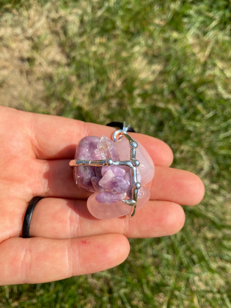 May include: A silver wire cage pendant with a pink and purple amethyst crystal cluster. The cage is adorned with small silver beads.