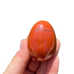 Op de afbeelding: Een glad, gepolijst rood jaspis ei met een hartvormig patroon. Het ei wordt in een hand gehouden.