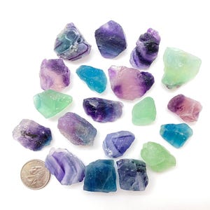 Puede incluir: Una colecci&oacute;n de 17 cristales de fluorita en varios tonos de verde, azul, morado y rosa. Los cristales son &aacute;speros y tienen un aspecto natural sin pulir.
