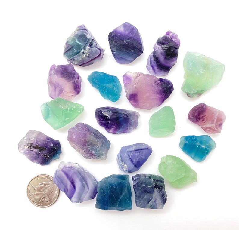 Puede incluir: Una colecci&oacute;n de 17 cristales de fluorita en varios tonos de verde, azul, morado y rosa. Los cristales son &aacute;speros y tienen un aspecto natural sin pulir.