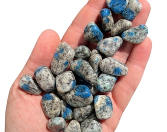 May include: A pile of blue and gray kyanite tumbled stones in a person's hand.