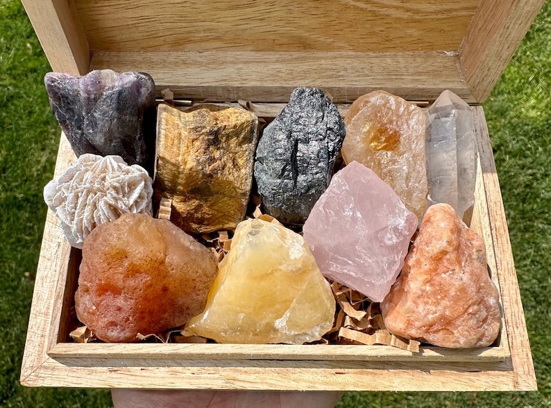 May include: A wooden box filled with a variety of colorful crystals and stones, including amethyst, tiger's eye, black obsidian, rose quartz, clear quartz, selenite, and carnelian.