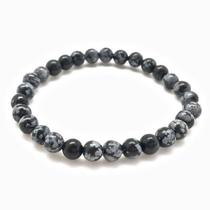 May include: A black and white snowflake obsidian beaded bracelet. The bracelet is made of round beads with a speckled pattern.
