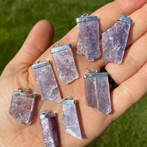 May include: Eight silver pendant charms with raw, purple lepidolite crystals. The crystals are all different shapes and sizes, but they are all roughly rectangular.