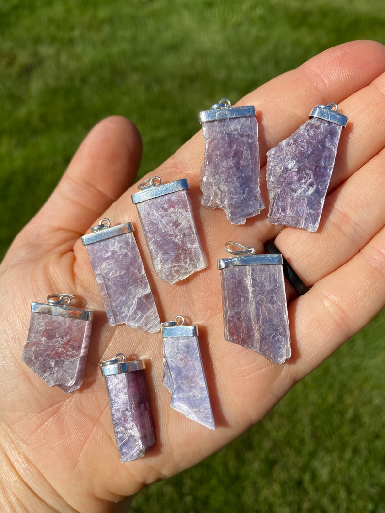 May include: Eight silver pendant charms with raw, purple lepidolite crystals. The crystals are all different shapes and sizes, but they are all roughly rectangular.