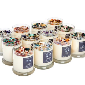 May include: Twelve glass candle jars with a white wax base and colorful crystals and glitter embedded in the wax. Each jar has a label with a zodiac sign and the corresponding month. The signs are Aries, Taurus, Gemini, Cancer, Leo, Virgo, Libra, Scorpio, Sagittarius, Capricorn, Aquarius, and Pisces.