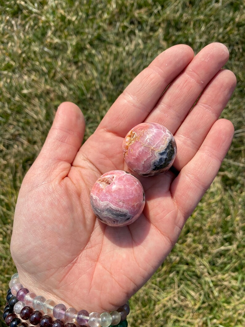 May include: Two pink and black, round, polished, gemstone spheres. The spheres are smooth and have a swirling pattern.