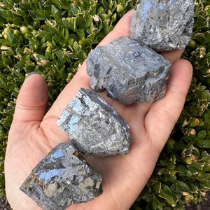May include: Four raw, gray, metallic, crystal specimens with a silvery sheen. The crystals are rough and have a layered, striated texture.