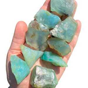 Puede incluir: Un pu&ntilde;ado de piedras preciosas en bruto de color aguamarina. Las piedras var&iacute;an en tama&ntilde;o y forma, con una calidad transl&uacute;cida. Algunas piezas tienen toques de marr&oacute;n y blanco. Las piedras preciosas se sostienen en una mano abierta.