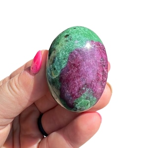May include: A smooth, oval-shaped green and pink gemstone with a polished finish. The stone has a swirling pattern of green and pink.