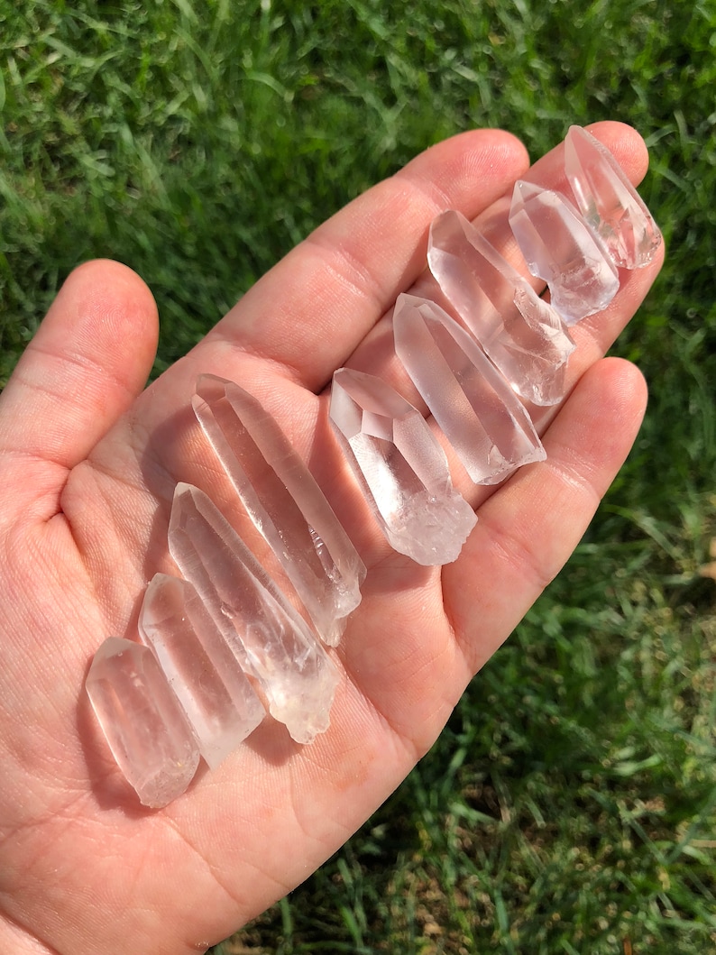 May include: A collection of ten clear quartz crystal points of varying sizes, displayed in a hand.
