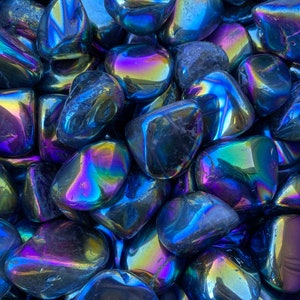 May include: A close-up of a collection of iridescent black obsidian tumbled stones. The stones have a smooth, polished surface and reflect a variety of colors, including blue, purple, and green.