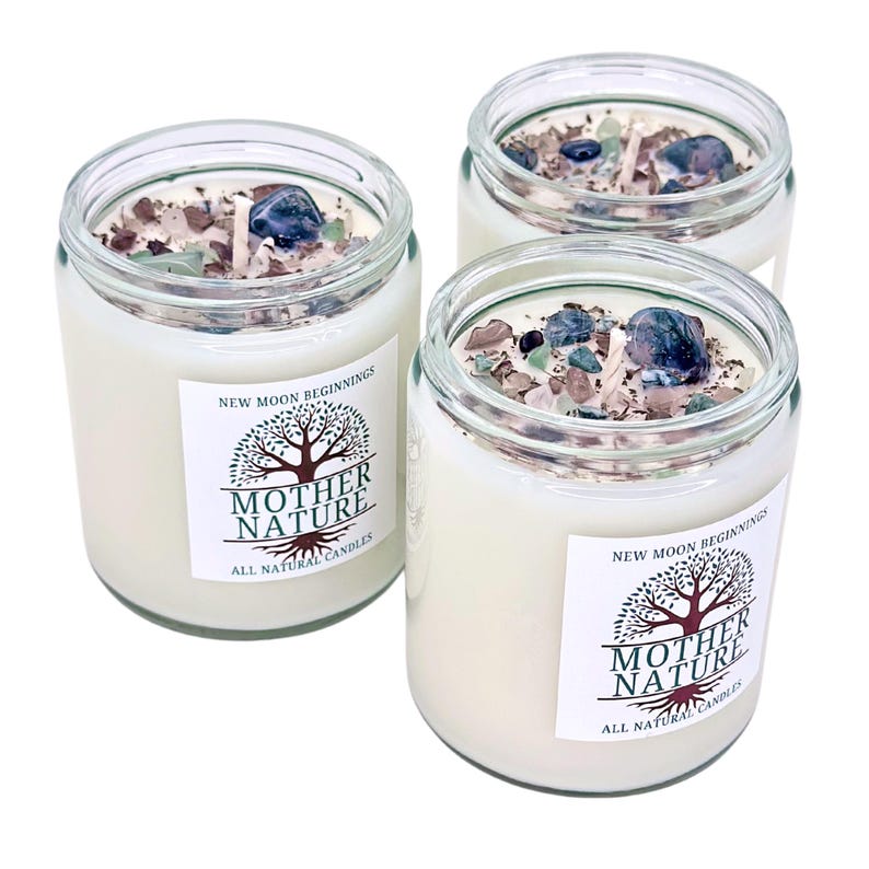 May include: Three glass jars with white candles and crystals inside. The jars have labels that say "New Moon Beginnings" and "Mother Nature All Natural Candles".