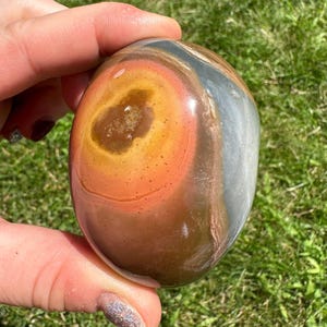 May include: A polished, multi-colored, round, natural stone with a large, orange, brown, and red center surrounded by a gray and white outer ring.