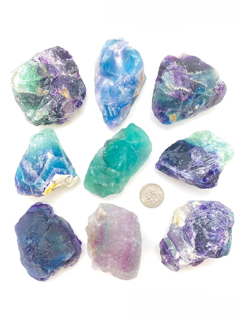 Puede incluir: Diez cristales de fluorita en varios tonos de azul, verde, morado y blanco. Los cristales son &aacute;speros y tienen un aspecto natural sin pulir. Se incluye una moneda de 20 c&eacute;ntimos de euro para la escala.